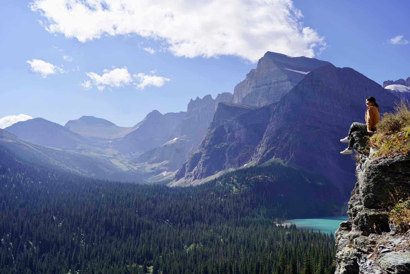 A photo of a YSEALI participant sitting on the edge of a rock face looking out over Glacier National Park
