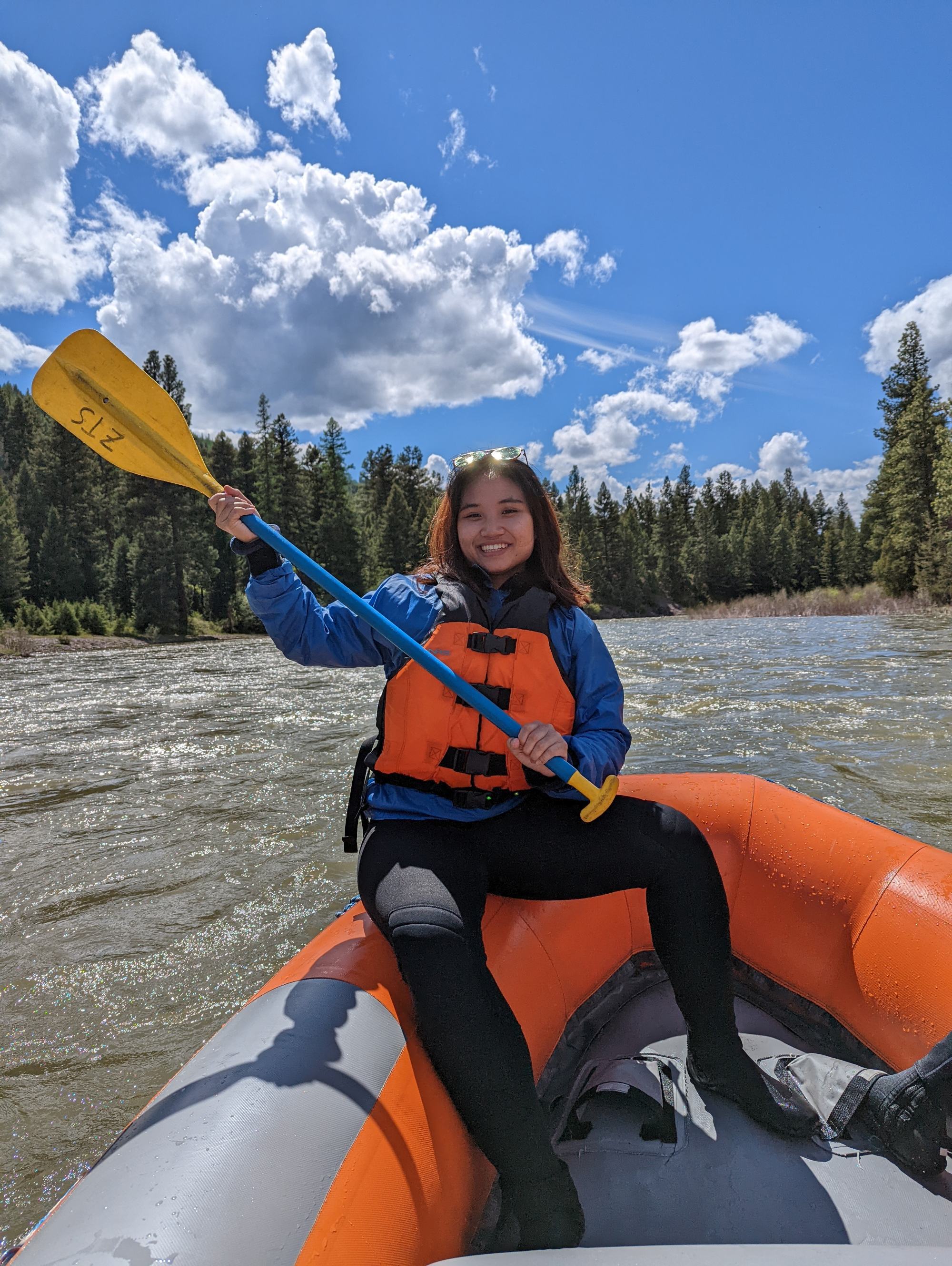A YSEALI participant sitting on the front of an orange raft with an orange life jacket on while holding a paddle.